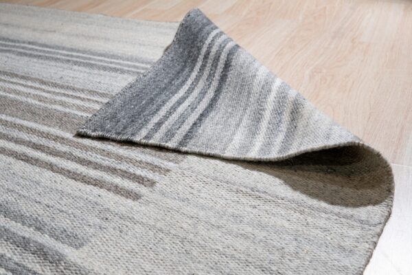 A gray and cream striped flatweave rug is partially folded back on a light wood floor.