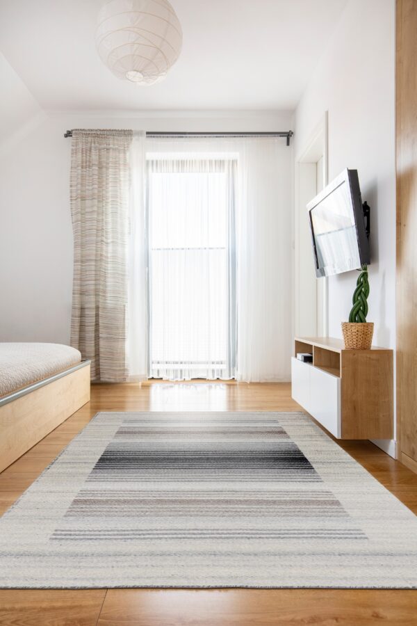 White, gray, and brown striped flatweave rug centered on light wood flooring in a bright modern room.