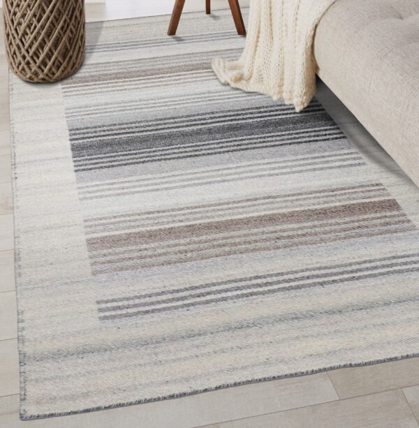 Flatweave rug featuring blocks of thin charcoal, taupe, and cream horizontal stripes on wood flooring.