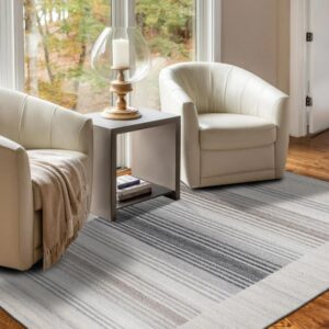 A gray and taupe striped rug sits on a hardwood floor between two cream chairs and a large window.