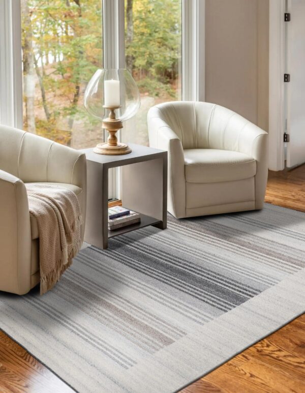 A gray and taupe striped rug sits on a hardwood floor between two cream chairs and a large window.