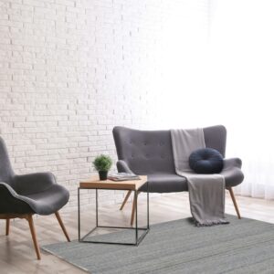 Textured gray rug beneath gray modern seating against a bright white brick wall and wood floor.