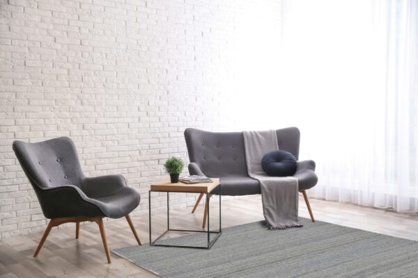 Textured gray rug beneath gray modern seating against a bright white brick wall and wood floor.