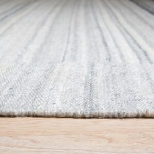 Close-up of a nubby, striped white and gray rug edge resting directly on light blonde wood flooring.