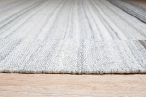 Close-up of a nubby, striped white and gray rug edge resting directly on light blonde wood flooring.