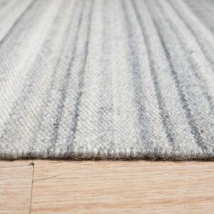 Extreme close-up of a textured light gray striped rug edge resting on a light wood plank floor.