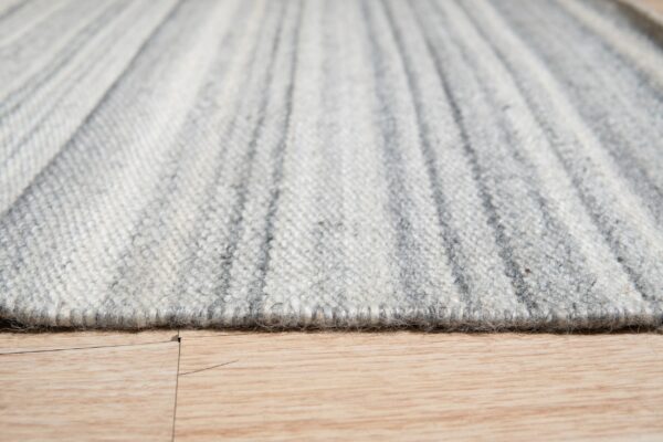 Extreme close-up of a textured light gray striped rug edge resting on a light wood plank floor.