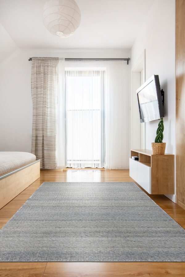 Gray and white woven texture rug centered on hardwood flooring in a bright modern room.