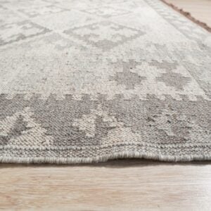 A low-angle view of a textured gray and cream rug with geometric patterns resting on light wood flooring.