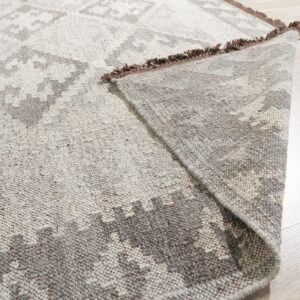 The corner of a low pile gray and beige geometric rug is folded back on light wood flooring.