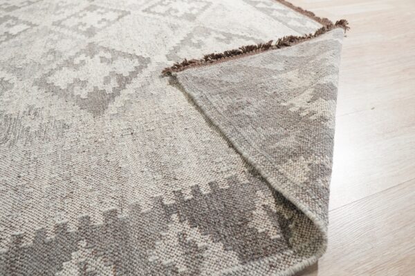 The corner of a low pile gray and beige geometric rug is folded back on light wood flooring.