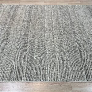 Black and light gray textured rug with a dense chevron pattern on wood plank flooring.