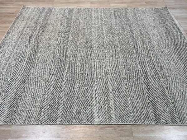 Black and light gray textured rug with a dense chevron pattern on wood plank flooring.