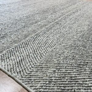 Textured gray and cream rug displaying a subtle chevron pattern, laid diagonally on light wood flooring.