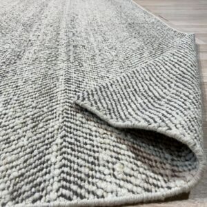 Heavily textured gray and white chevron rug, partially rolled, resting on light-colored wood flooring.