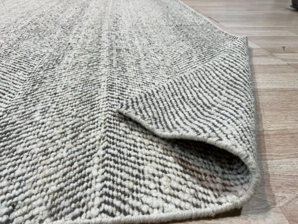 Heavily textured gray and white chevron rug, partially rolled, resting on light-colored wood flooring.