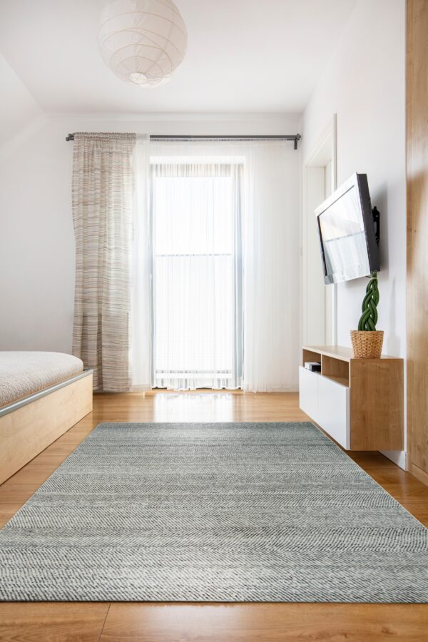 Low-pile gray and white chevron rug placed on wood flooring in a bright minimalist room near a bed.