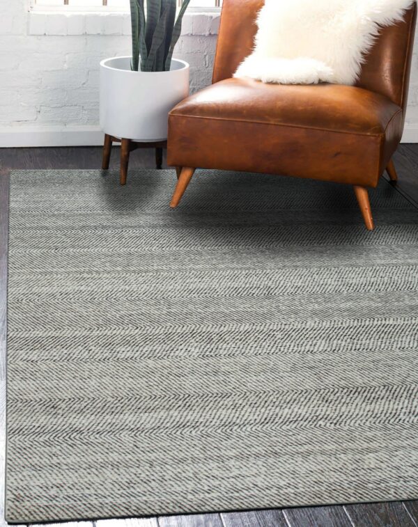 Light and dark gray chevron rug on wood flooring, next to a brown leather chair and houseplant.