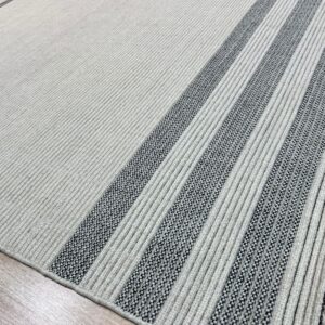 Ribbed light-colored rug with thick black and white stripes and visible fringe on wood floor.