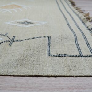 Textured beige rug with black, white, and tan geometric patterns, dark fringe, resting on wood flooring.