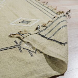 A beige rug with black and white geometric embroidery is folded over a light wood floor.