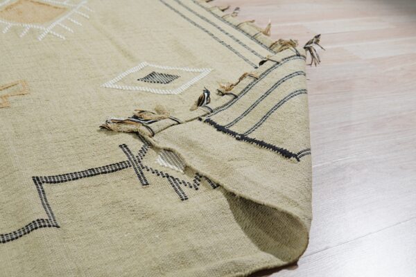 A beige rug with black and white geometric embroidery is folded over a light wood floor.