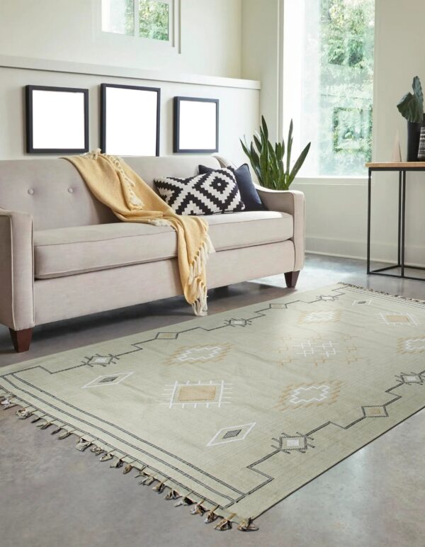 A light green flatweave rug featuring geometric patterns lays beneath a sofa in a bright room.