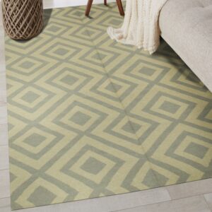 Low-pile rug with geometric diamond pattern in sage and beige on light wood flooring.