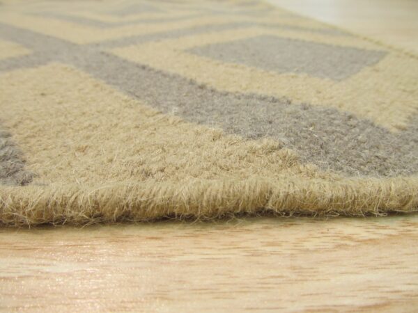 Close-up of a shaggy beige and gray geometric rug edge on a glossy light wood floor.
