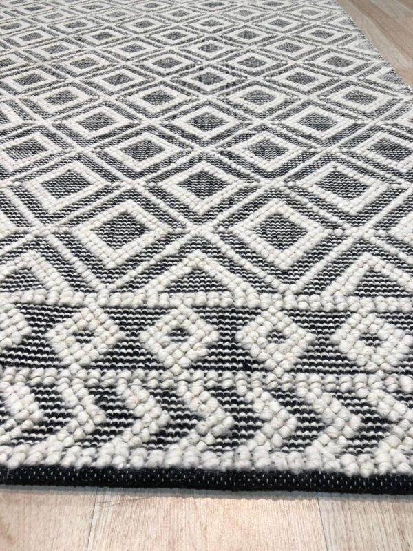 Textured black and white diamond pattern rug featuring contrasting flat and raised pile on light wood planks.