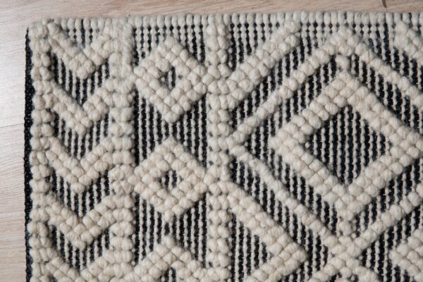 Textured black and off-white rug displaying a chunky geometric diamond pattern on a light wood floor.
