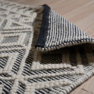 Cream and black textured diamond rug, partially rolled, rests on light beige wood flooring.