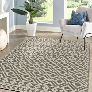 Black and beige flatwoven diamond rug on chevron floor, next to a gray armchair and a large window.