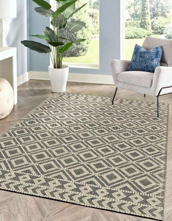 Black and beige flatwoven diamond rug on chevron floor, next to a gray armchair and a large window.