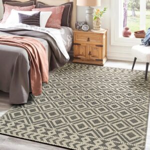 A black and cream geometric flatweave rug anchors a bright bedroom with gray flooring and wood furniture.