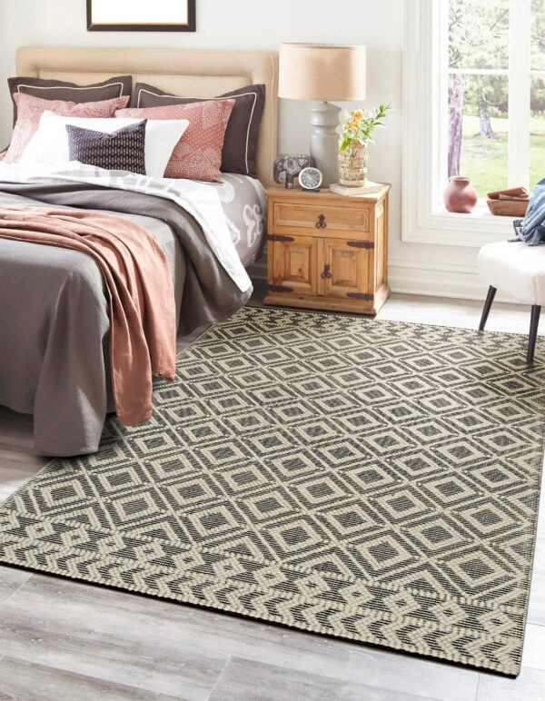 A black and cream geometric flatweave rug anchors a bright bedroom with gray flooring and wood furniture.
