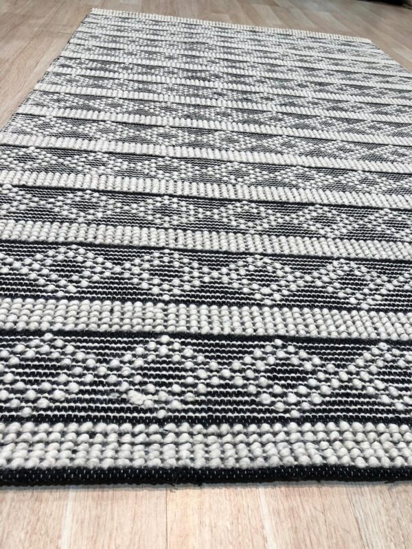 Black and white textured striped rug featuring raised knots on light wood plank flooring.