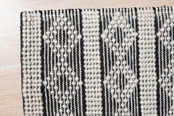 Black and white striped rug with a chunky, raised knot texture lies on light wood flooring.