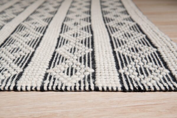 Textured black and white striped rug with raised patterns lies on light wood flooring.