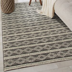 A black and cream flatwoven rug with horizontal stripes and geometric patterns covers light wood flooring.