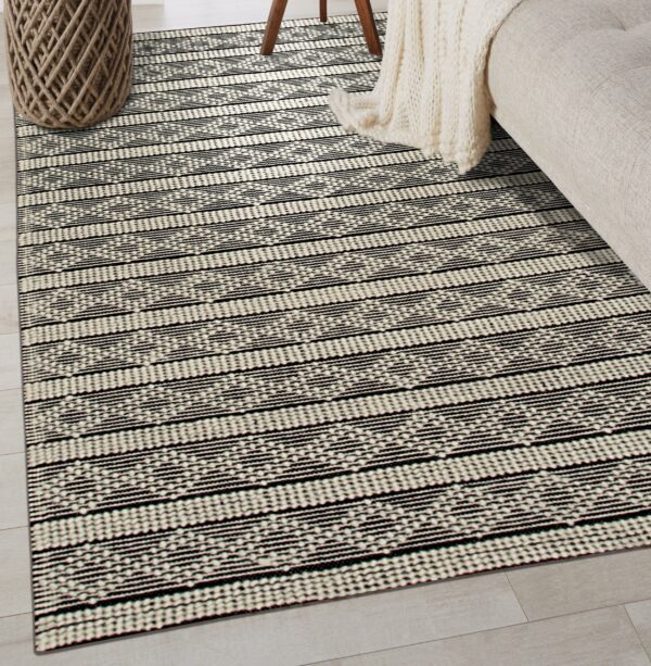 A black and cream flatwoven rug with horizontal stripes and geometric patterns covers light wood flooring.