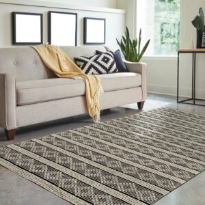A flatweave black and white geometric patterned rug lies on concrete flooring beneath a neutral sofa.