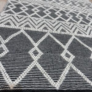 Black and white rug with raised geometric diamonds and chevrons on light wood plank flooring.