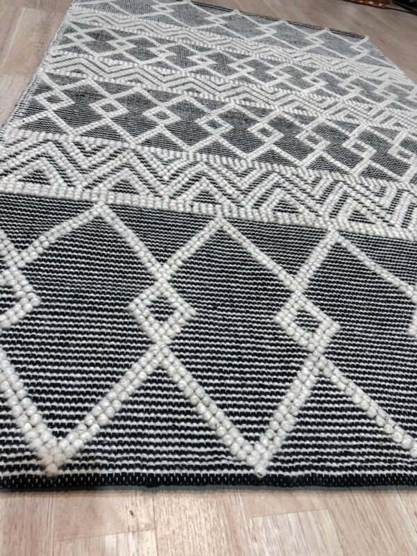 Black and white rug with raised geometric diamonds and chevrons on light wood plank flooring.