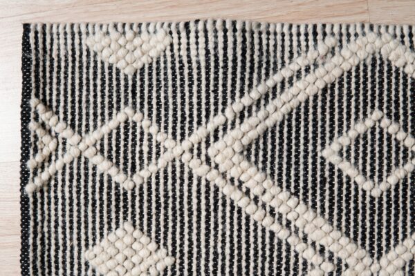 Black and white rug texture showing vertical stripes and raised off-white geometric patterns on wood floor.