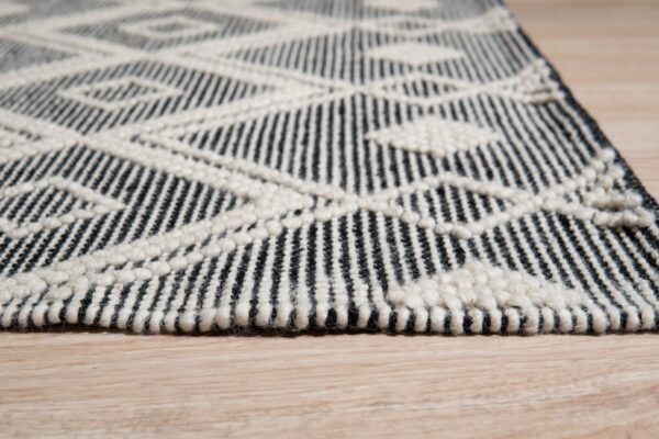 Black and cream geometric rug with textured loop accents rests on light wood flooring.