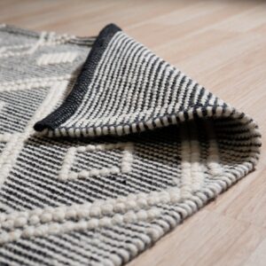 Black and white textured geometric rug detail, partially rolled back on light blonde wood flooring.