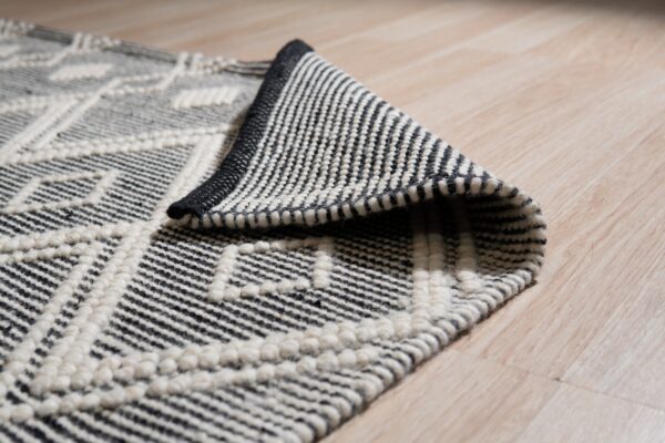 Black and white textured geometric rug detail, partially rolled back on light blonde wood flooring.
