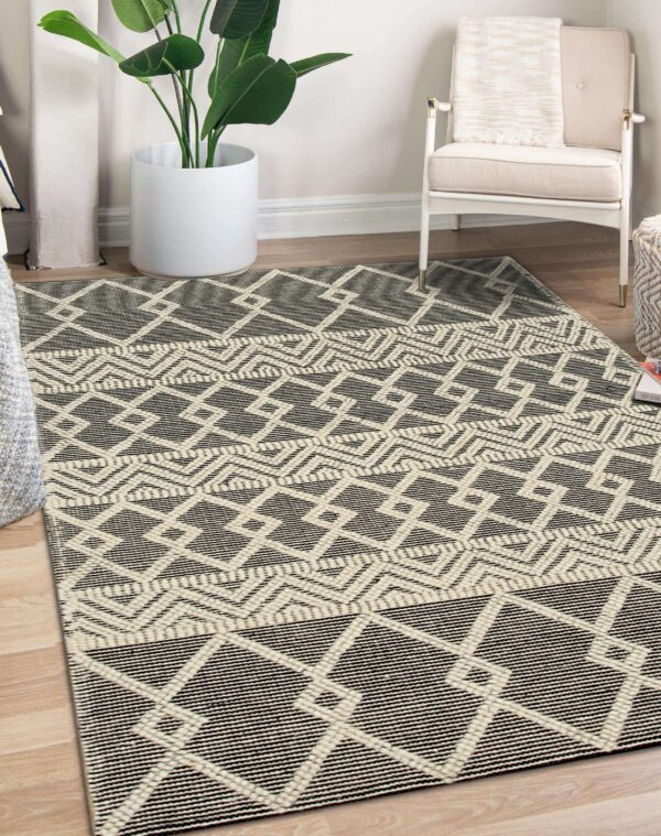 Geometric cream and dark gray flatwoven rug beneath a white chair and large indoor plant.