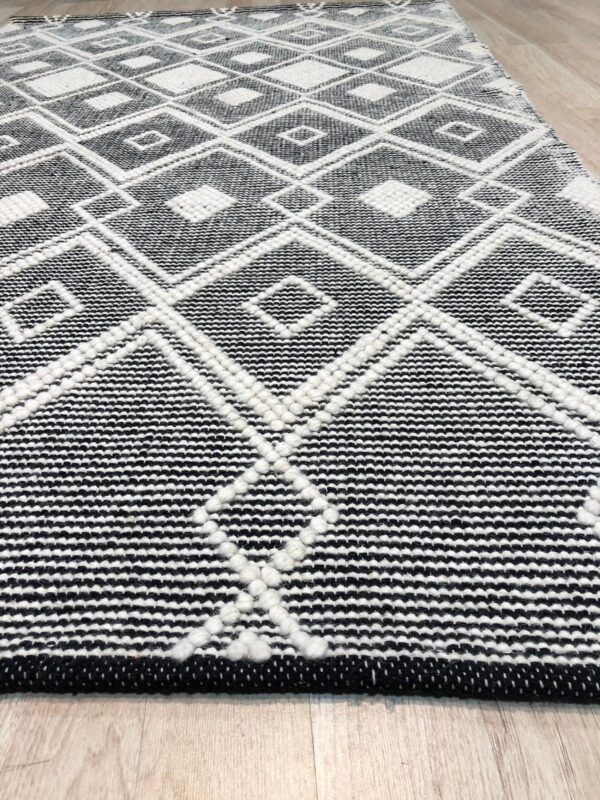 Black and white geometric rug with raised white diamond patterns lying on light wood floor.